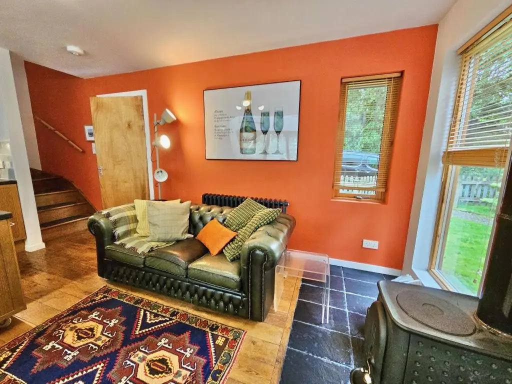 a living room with a leather couch and orange wall at Baltinna East - by Where Stags Roar in Newtonmore