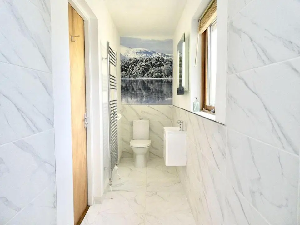 a white bathroom with a toilet and a window at Baltinna East - by Where Stags Roar in Newtonmore