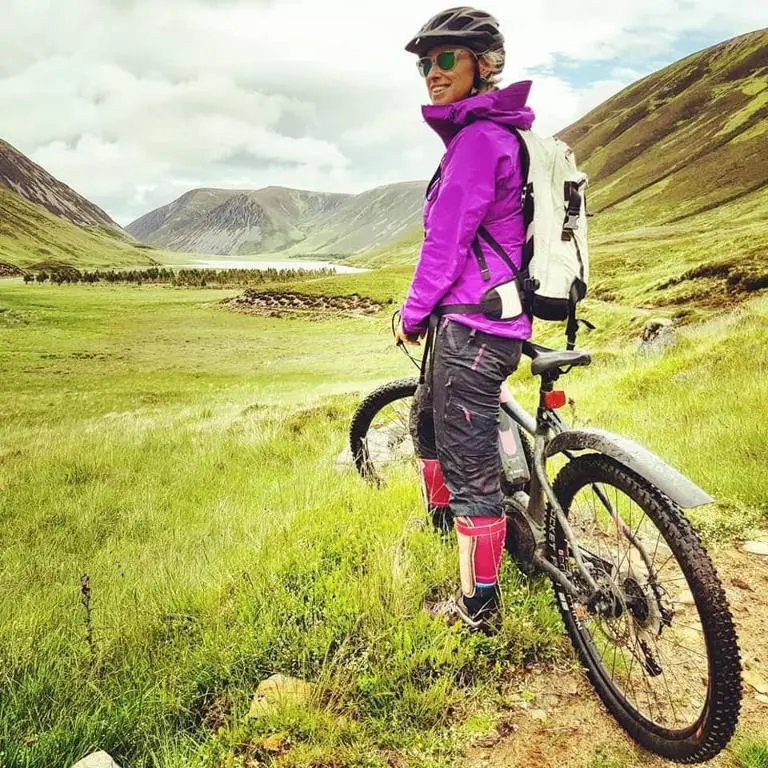 a woman standing next to a bike on a hill at The Byre - by Where Stags Roar in Newtonmore