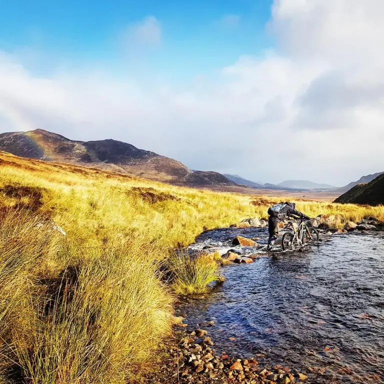 a person is crossing a stream in a field at The Bakehouse - by Where Stags Roar in Newtonmore