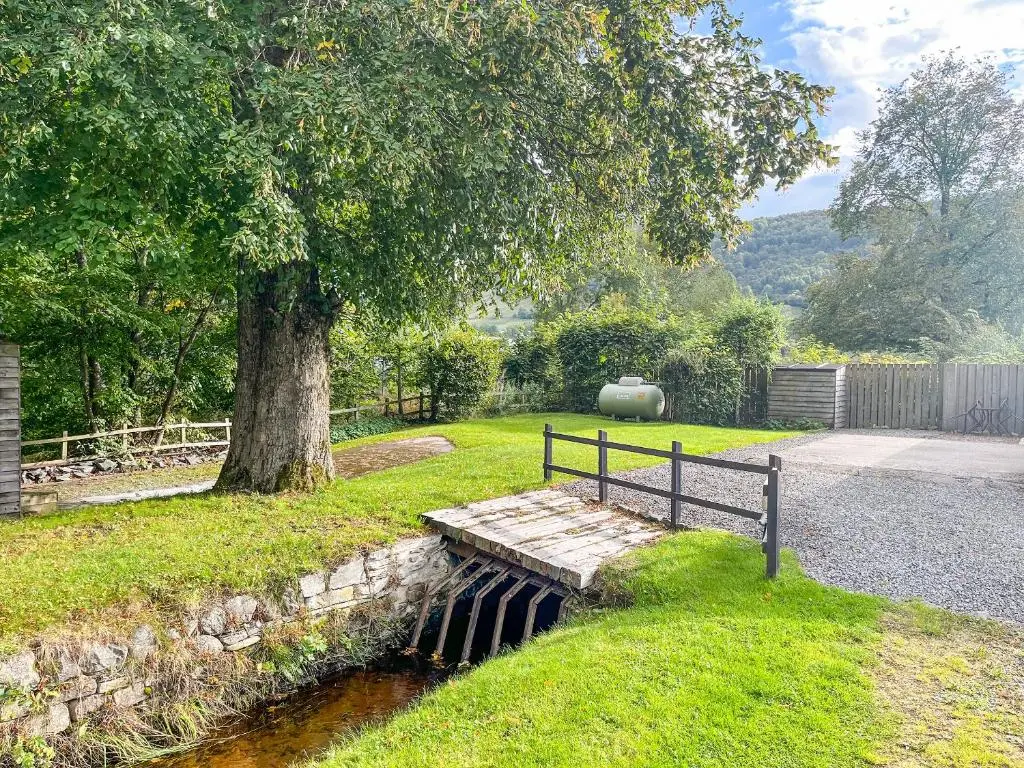 a bench sitting next to a tree next to a river at Old Mill Cottage in Blair Atholl
