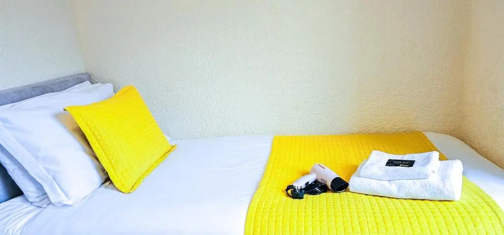 a bed with a yellow blanket and a towel and a camera at mySTAYINN Telford 7 Bedroom House in Inverness