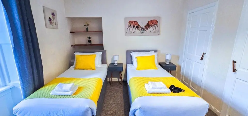 two twin beds in a small room with yellow pillows at mySTAYINN Telford 7 Bedroom House in Inverness