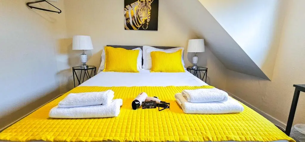 a yellow bed with two towels and a camera on it at mySTAYINN Telford 7 Bedroom House in Inverness