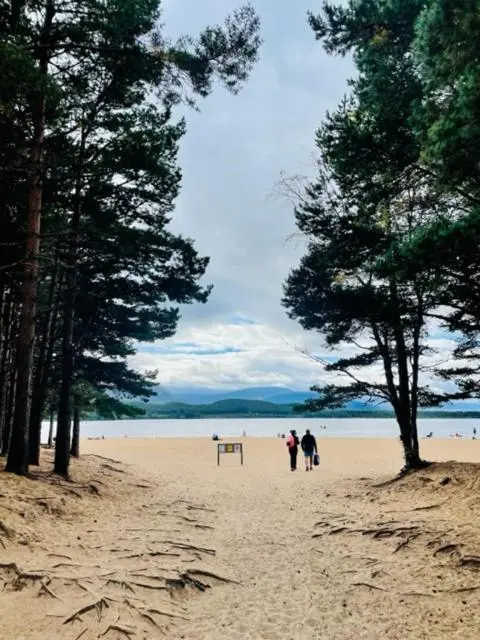 two people walking on a sandy beach with trees at Tom's Lodge in Boat of Garten