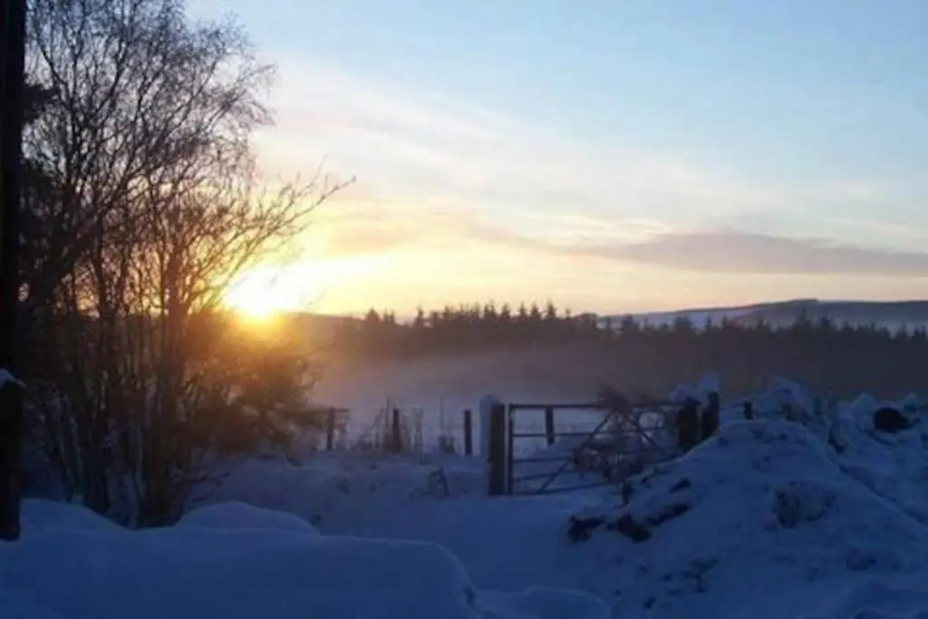 a snowy field with the sun setting in the background at Red Squirrel log cabin with hot tub in Keith