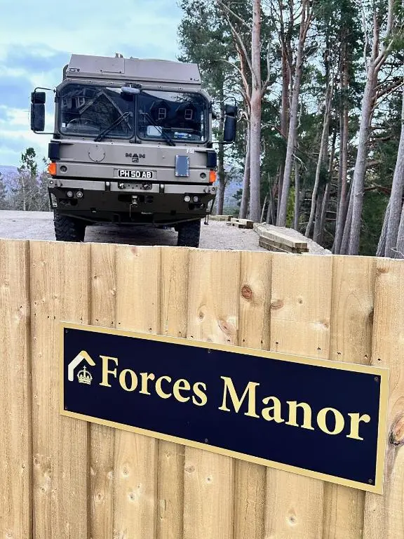 a truck parked behind a fence with a forest manor sign at Forces Manor in Kincraig