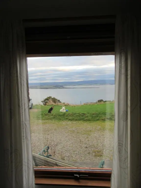a window with a view of a field and water at Kestrel, Longhouse Cottages in Rosemarkie