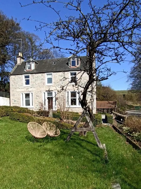 a house with two chairs in the grass in front of it at Abbeyfield B&B in Dufftown