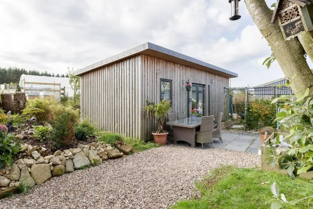 a small shed with a table in a garden at Cosy and modern 1 bedroom garden house - very dog friendly! in Tarves