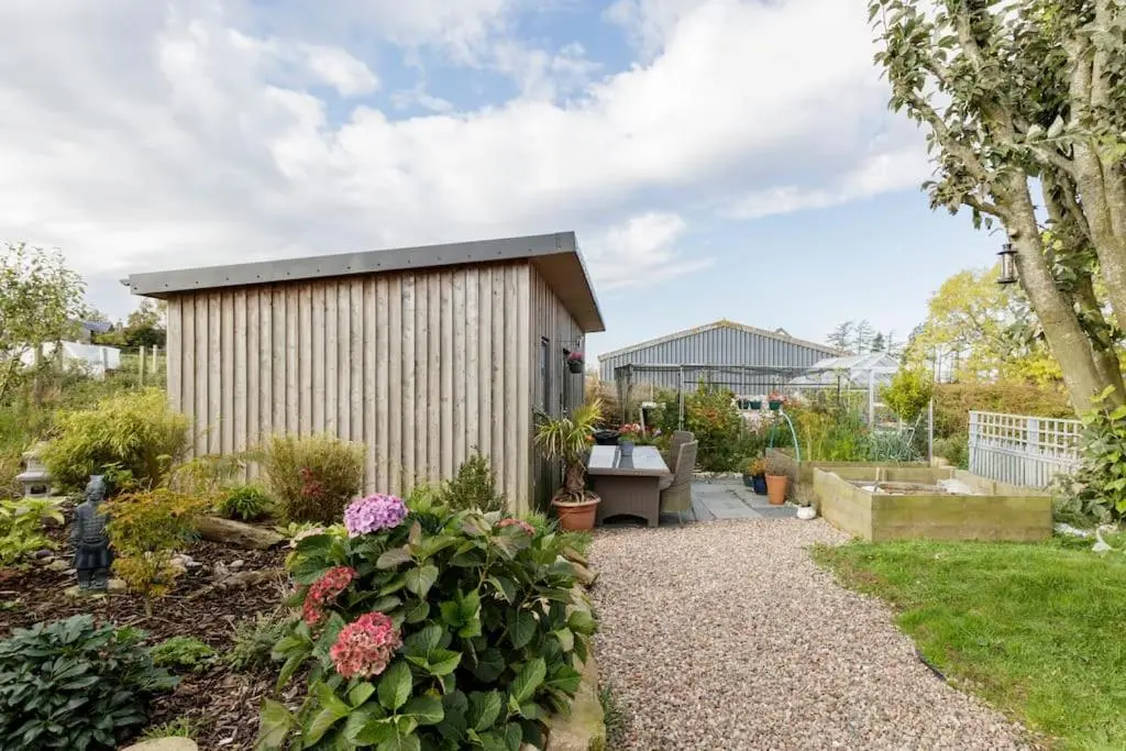 a garden with a shed and some flowers at Cosy and modern 1 bedroom garden house - very dog friendly! in Tarves