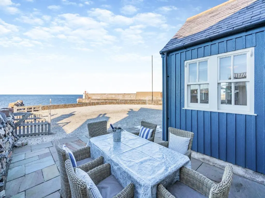 a blue house with a table and chairs and the ocean at The Old Net Shed in Whitehills