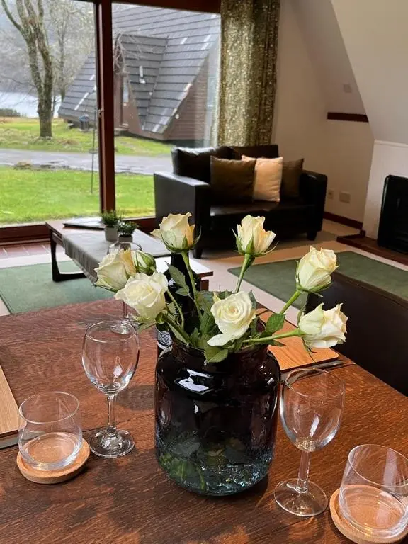 a vase with white roses on a table with wine glasses at Caledonia Lodge in Spean Bridge