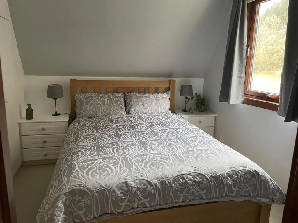 a bedroom with a bed with a white comforter and a window at Caledonia Lodge in Spean Bridge