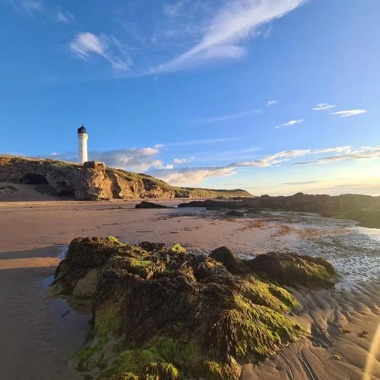 a view of a beach with a lighthouse in the distance at Lyons Retreat in Lossiemouth