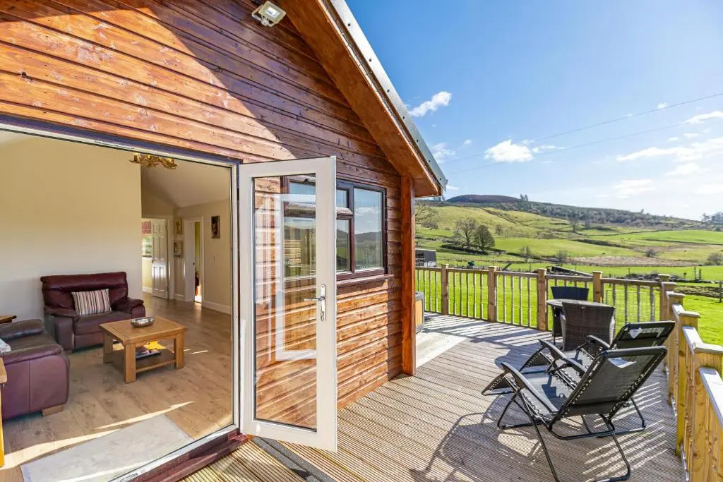 a house with a deck with a couch and chairs at Pine Marten Lodge with Hot Tub in Cray