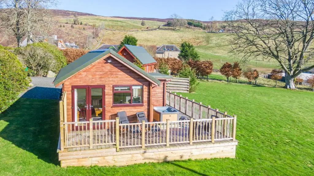 a wooden cabin in a field with a fence at Pine Marten Lodge with Hot Tub in Cray