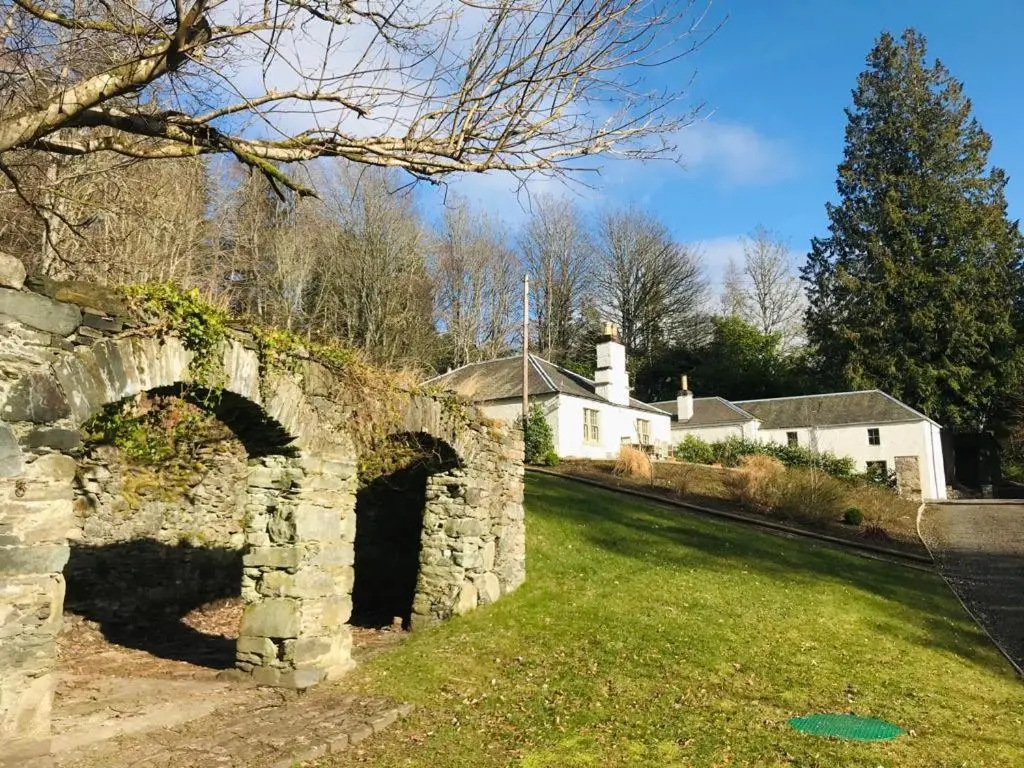 an old stone bridge in a field with a house at Gardeners cottage in Pitlochry