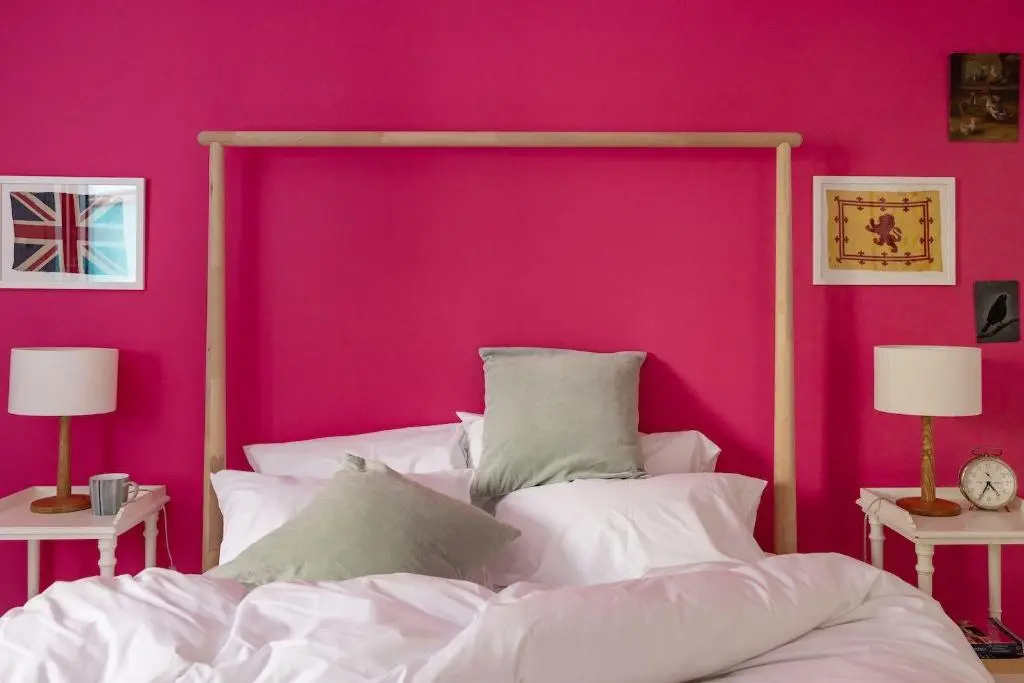a bedroom with a pink wall and a bed with pillows at Number 4 Steading Cottage in Banchory