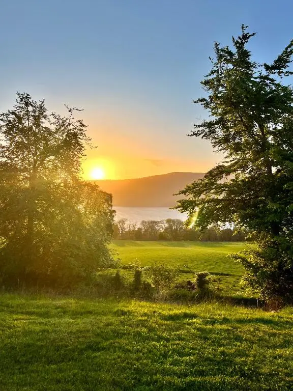 a sunset over a field with trees in the foreground at 1 Loch Ness Heights in Inverness
