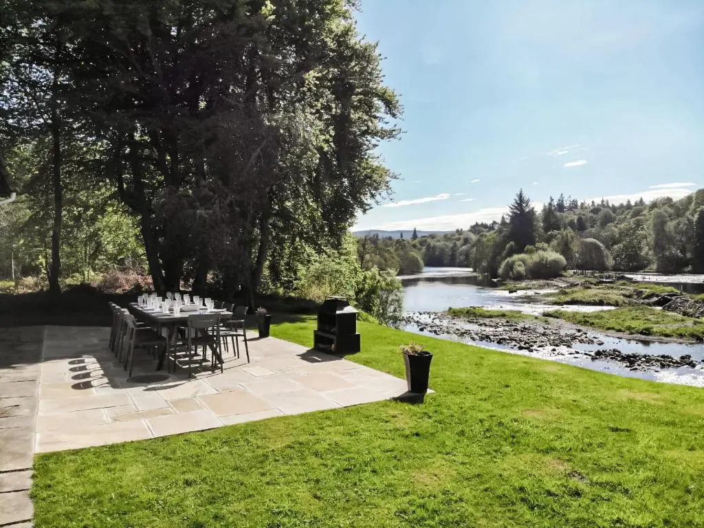 a picnic table in the grass next to a river at Cruives Lodge in Kiltarlty