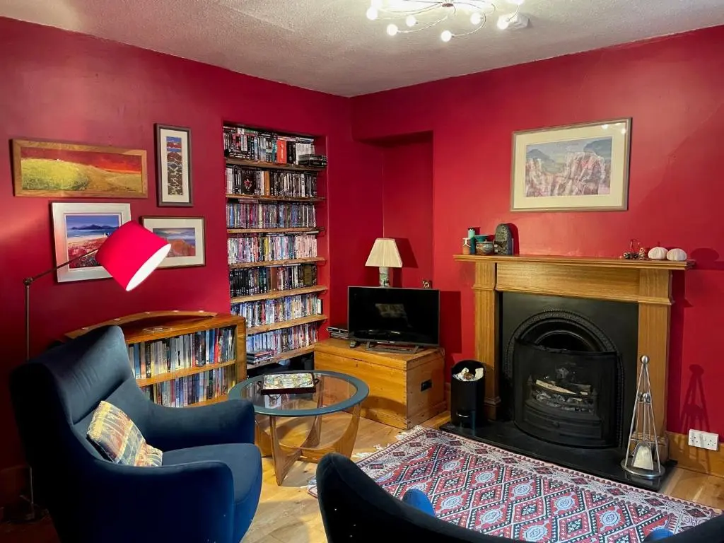 a living room with a fireplace and a red wall at One bed cosy Highland cottage near Beauly in Beauly