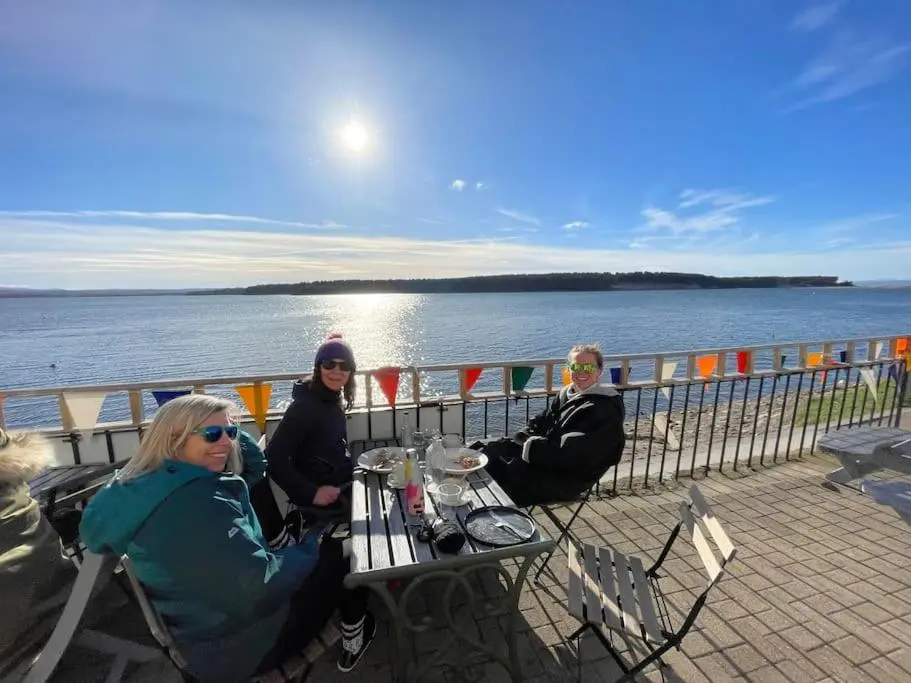 a group of people sitting at a table by the water at Osprey Hide in Forres