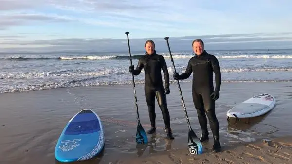 two men in wet suits standing on the beach with their surfboards at Driftwood Cottage, Findhorn Village in Forres