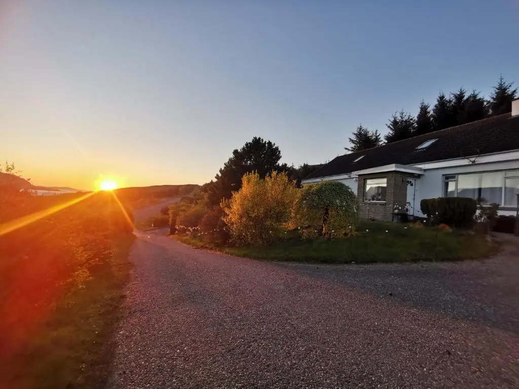 a house on a road with the sunset in the background at Lochbroom Lodge in Ullapool