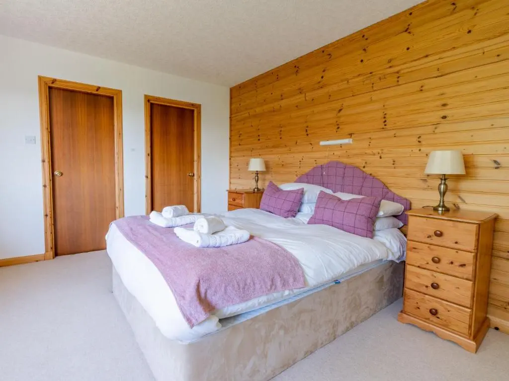 a bedroom with a large bed with a wooden wall at Holiday Home Achmony Secluded Westend by Interhome in Drumnadrochit