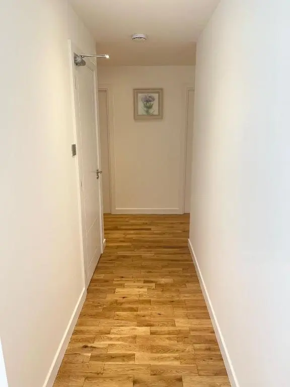 an empty hallway with a wooden floor and white walls at Inverness Highland Apartment in Inverness